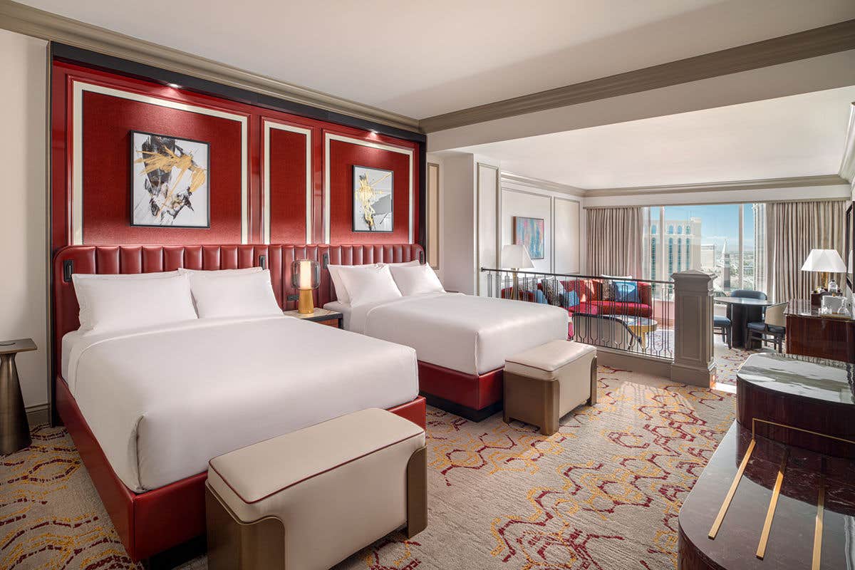 Luxurious hotel room with two beds, red leather headboards, and abstract artwork above. City view in the background.