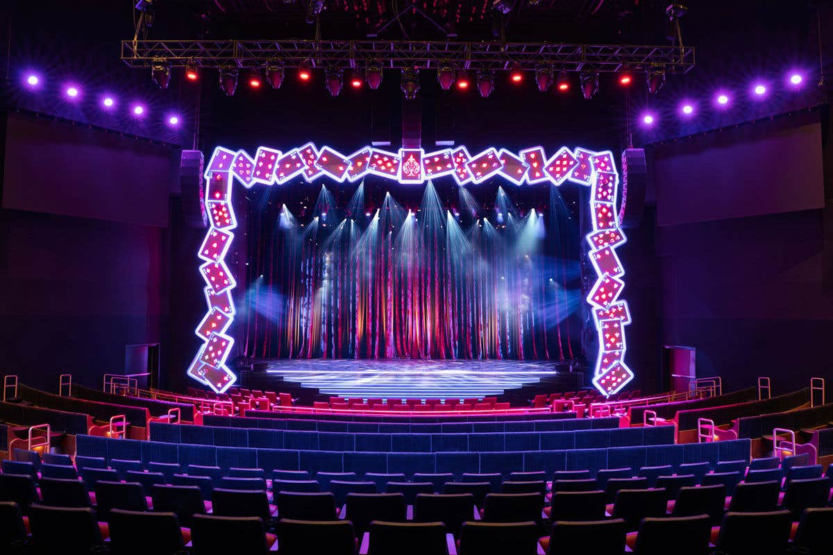 Palazzo Theatre stage framed with illuminated oversized playing cards, casting colorful beams onto the shimmering curtain.