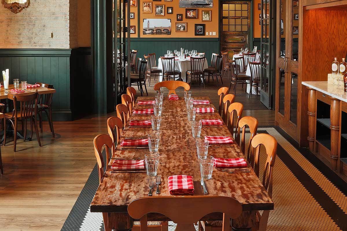 Long dining table with red checkered napkins in a rustic restaurant setting with framed photos on the walls.