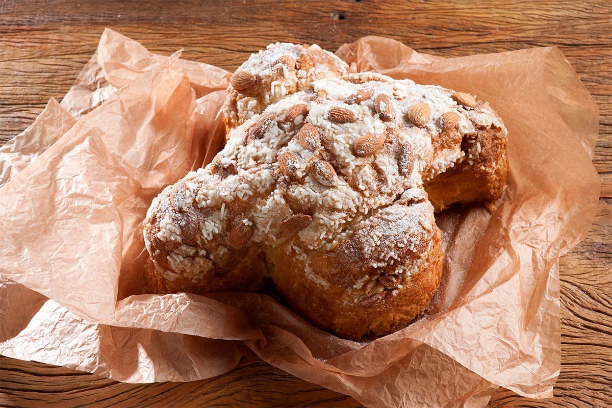 A traditional Italian Easter dove cake (Colomba Pasquale) with powdered sugar and almonds on crinkled parchment paper.