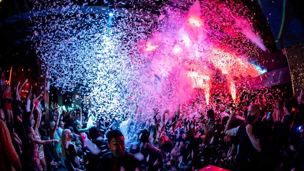 A crowded nightclub with colorful lights and beams illuminating people dancing.