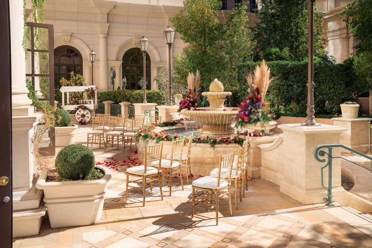 Elegant courtyard setup for an outdoor wedding ceremony with a fountain centerpiece surrounded by chairs and floral decorations.