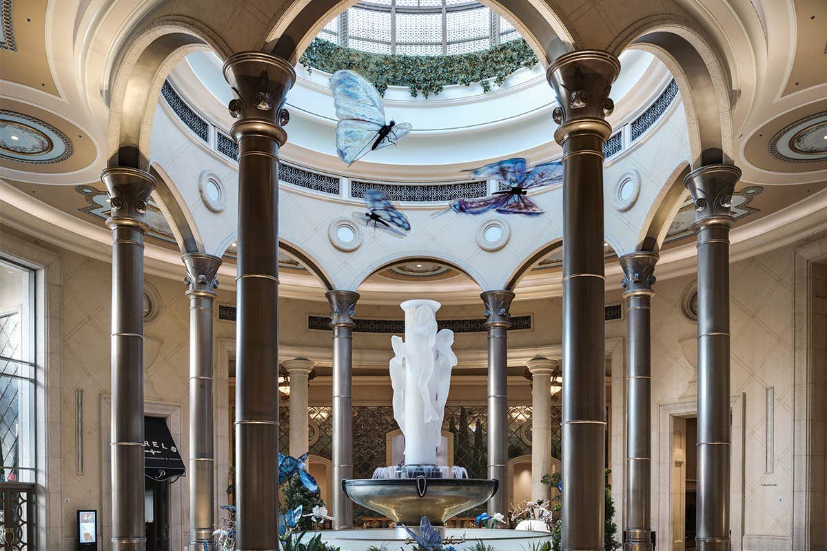 Elegant atrium with a central statue, surrounded by tall columns, ornate ceiling, and large butterfly sculptures above.