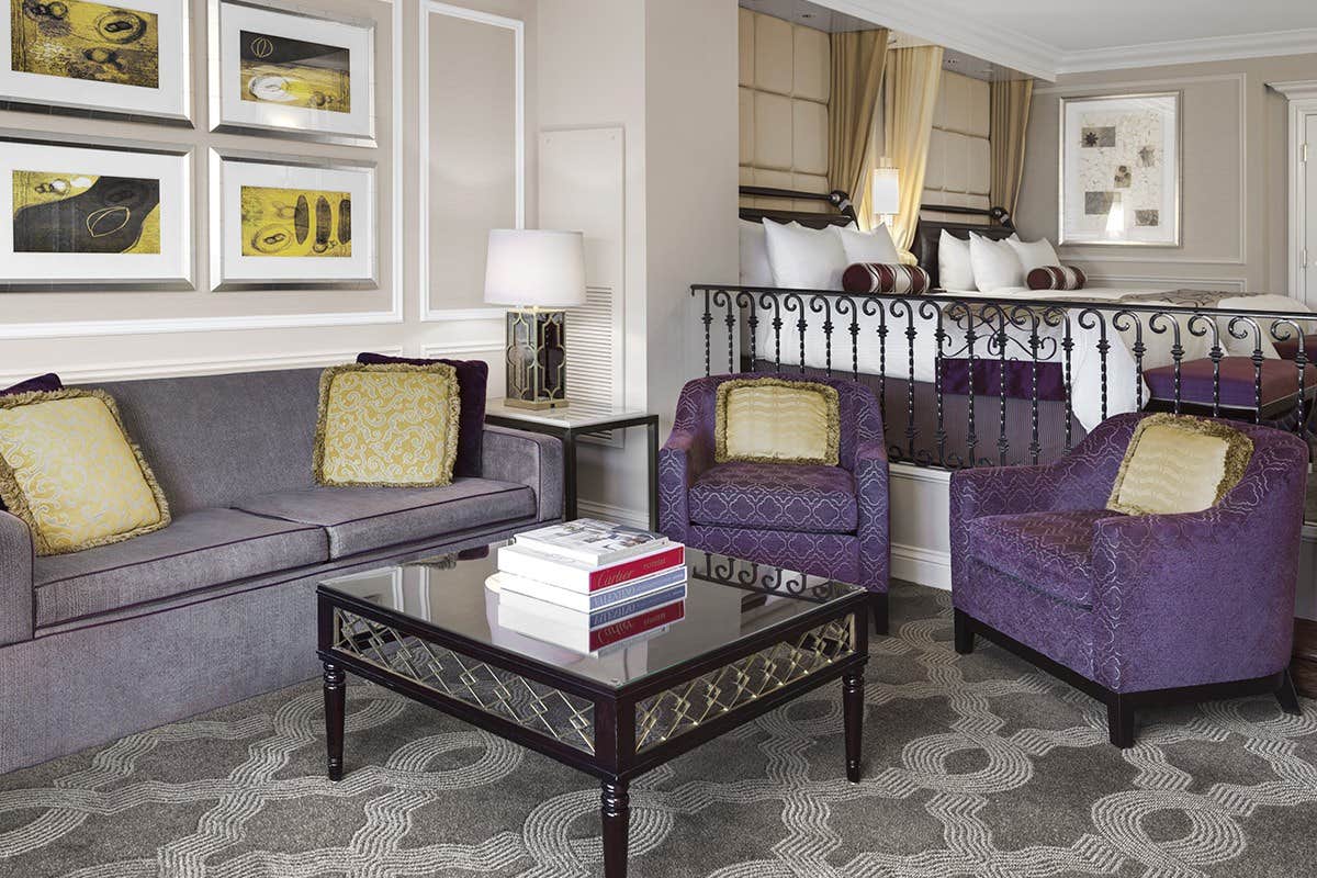 Elegant living area with two purple armchairs, a purple sofa, a glass coffee table, and framed artwork on the walls.