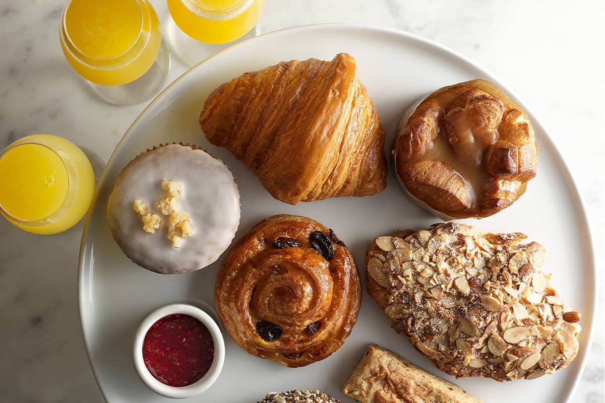 A plate with assorted pastries, a croissant, and glasses of orange juice on a marble surface.