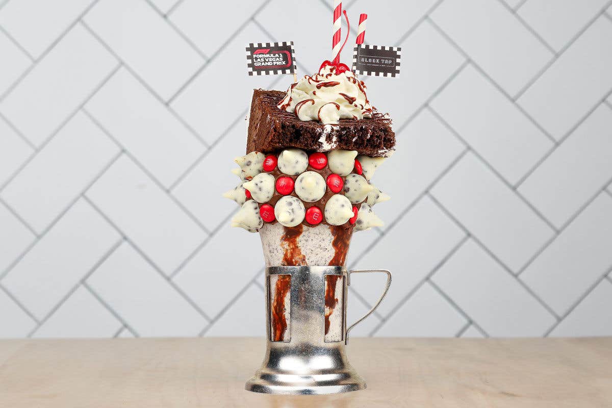 The Grand Prix CrazyShake™ OREO® Shake from Black Tap Craft Burgers & Beer made with a chocolate-frosted rim, cookies 'n cream Hershey Kisses, red M&M'S®, and is topped with a black-and-white cake slice, whipped cream, and a cherry