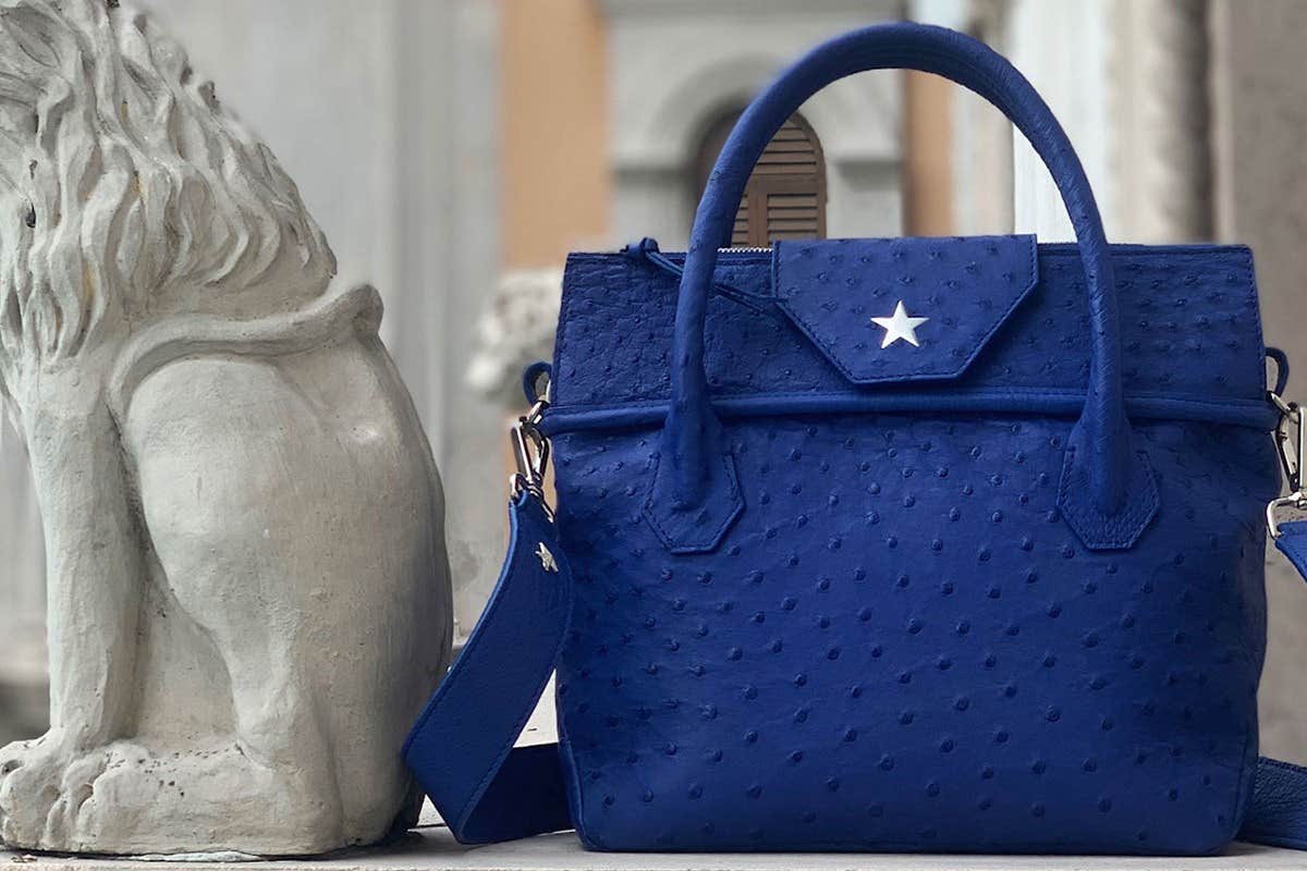 A blue textured handbag with a star emblem is placed next to a white stone lion statue.