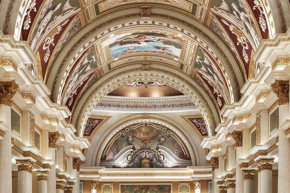 Ornate ceiling with intricate murals, arches, and columns in a grand hall, showcasing classical architecture and opulent details.